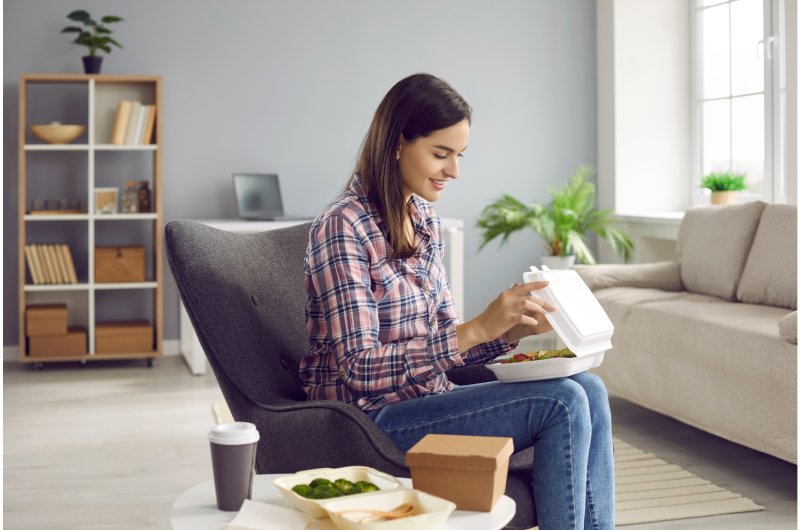 Mujer sentada en un sofá abriendo un pedido de comida con entrega a domicilio